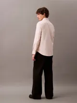 Camisa de manga larga color rosa claro, confeccionada en tejido Oxford de algodón y elastano. Presenta cuello camisero clásico, cierre frontal con botones y logo de Calvin Klein bordado en el pecho. Corte regular.