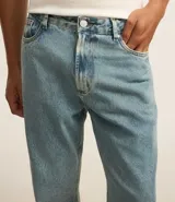 Pantalón de jean celeste con lavado dirty, corte flare, cintura fija con trabillas, cierre con botón y cremallera, y bolsillos.