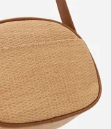 Cartera bandolera pequeña color beige con textura de paja y detalles en marrón. Tiene cierre de cremallera, bolsillo externo y asa larga regulable con hebilla.