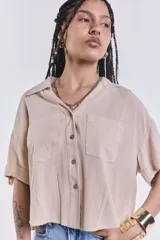 Camisa color beige de corte cropped, con cuello clásico, cierre frontal con botones y dos bolsillos de parche en el pecho.