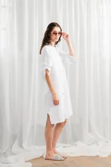 Túnica blanca de lino, corte holgado, con cuello mao, cierre frontal con botones y mangas largas con trabillas para enrollar.