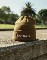 Gorro de lana sintética color marrón con bordado frontal de la frase "Risk takers" en color blanco.