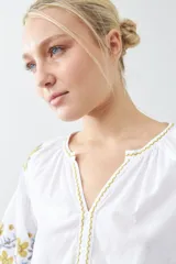 Blusa blanca de estilo boho con bordados de flores en amarillo y azul en mangas y escote.