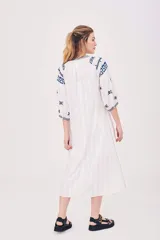 Vestido túnica blanco con bordados azules, mangas 3/4 y cuello con lazo ajustable.