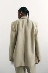 Blazer color beige de corte holgado con solapas de muesca, hombreras, abertura y botón en los puños, bolsillos delanteros ribeteados y bolsillo superior ribeteado. Forrado.