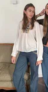 Pantalón de jean azul oscuro, de corte ancho y tiro bajo. Presenta cierre y botón en la parte delantera, bolsillos delanteros con detalle de encaje, bolsillo trasero y presillas para cinturón.