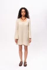 Vestido corto color crema, tejido de punto con lurex, escote redondo y mangas largas acampanadas.