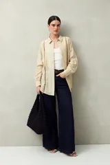 Camisa blanca de lino con botones de nácar, corte recto, cuello clásico y mangas largas con puños abotonados. Presenta detalles de calados tipo vainillas en el frente y las mangas.