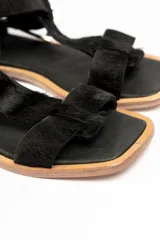 Sandalia plana negra de cuero con tira delantera y tira al tobillo con hebilla metálica plateada.