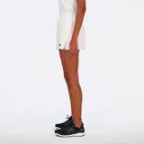 Conjunto deportivo New Balance de tenis para mujer, compuesto por un top sin mangas con cuello polo y una falda corta con cintura ancha. Ambos en color blanco con logo de la marca en azul marino.