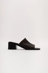 Sandalia marrón de cuero con punta cuadrada, talón abierto y faja ancha. Tiene detalle de elástico oculto en la cara interna de la capellada. El forro y la plantilla son de cuero vacuno.