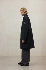 Chaqueta larga de color blanco roto, con cuello camisero y cierre frontal de broches. Presenta un corte holgado y bolsillos laterales.