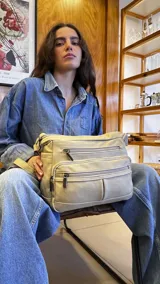 Bandolera de símil cuero color beige, con tres bolsillos frontales con cierre, un bolsillo trasero con cierre y bolsillos internos. Cuenta con una correa larga regulable.