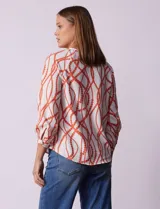 Blusa estampada blanca con diseño de cadenas y círculos color naranja. Cuello redondo con escote en V y lazo de ajuste. Manga 3/4.