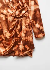 Vestido corto de poliéster con estampado tie-dye en tonos marrones y beige. Presenta cuello redondo, mangas largas, diseño cruzado con drapeado en la cintura y cierre de botón en la parte posterior.