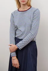 Remera de manga larga con diseño de rayas horizontales en azul y blanco, destacada por un cuello redondo en color bordó con costuras a la vista.