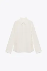 Camisa color blanco hueso de corte holgado, con cuello solapa, manga larga y cierre frontal con botones. Presenta detalle de botones en la cintura.