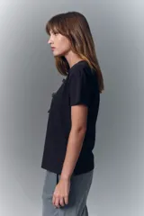 Remera negra de algodón con cuello redondo y mangas cortas. Presenta un estampado en el escote que simula un collar estilo boho con cuentas, borlas y dijes.