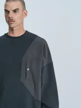 Buzo negro de cuello redondo, corte oversize y largo crop. Confeccionado en frisa gamuzada de algodón con recortes de microfibra y bolsillo delantero con cierre a presión.