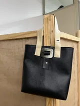 Bolso tipo tote bag negro con textura símil cuero de cocodrilo, doble asa corta de cuero marrón y beige, y cierre con broche metálico con forma orgánica.