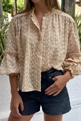 Camisa color beige con bordado de flores blancas, cuello con volados y mangas 3/4 abullonadas con puños elásticos.