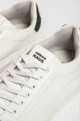 Zapatillas urbanas blancas de cuero sintético con cordones y detalle negro en el talón.