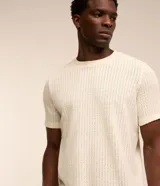 Remera de hombre color crudo, de punto calado con textura de encaje, cuello redondo y mangas cortas. Corte regular. Confeccionada en poliéster y algodón.
