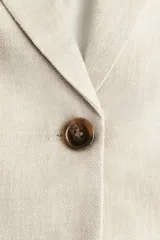 Blazer color beige de lino y viscosa, con solapas de pico, hombreras finas, cierre de un botón, pinzas en la cintura, abertura con botón en los puños, bolsillos delanteros ribeteados y abertura atrás.