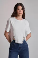 Remera blanca de algodón con cuello redondo y mangas cortas. Presenta apliques de strass en los laterales del ruedo.