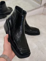 Bota de charol negra con punta cuadrada, tacón grueso y cierre lateral.