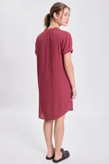 Vestido corto color bordó, de manga corta y escote en V con cuello mao. Presenta un corte holgado con pliegues verticales en la parte delantera.
