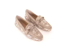 Mocasín de cuero gamuzado color avena, con bordados contrastantes, apliques metálicos y lazo decorativo en la capellada.