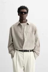 Camisa color crema de corte relaxed fit, confeccionada en tejido de mezcla de algodón suave al tacto. Tiene cuello solapa, manga larga con puños abotonados, un bolsillo de parche en el pecho y cierre frontal con botones.