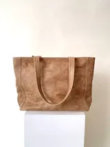 Cartera tipo tote de cuero graneado color negro, con textura uniforme y suave al tacto. Tiene manijas de 55 cm, bolsillo frontal con broche imantado, bolsillo trasero con cierre metálico, cierre principal metálico, forro interior y tres bolsillos internos (uno con cierre, uno plaqué y uno tipo sobre con solapa y botón).