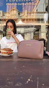 Bandolera pequeña de textura símil cuero color caramelo/marrón, con dos compartimentos principales con cierre. Correa ancha ajustable de tela negra con inscripción en relieve.