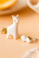 Par de aros de cerámica blanca con forma de esfera y detalle dorado en la parte superior. Cierre con tuerca a presión.