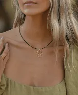 Collar con cordón de cuero negro y dije dorado con forma de círculos concéntricos.