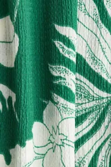 Pantalón ancho de punto con estampado floral blanco sobre fondo verde. Tiene tiro alto, cintura elástica y piernas amplias.