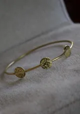 Pulsera rígida dorada con tres apliques circulares con textura martillada.