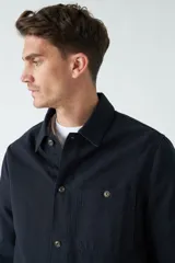 Sobrecamisa verde militar de algodón grueso tipo canvas, con cuello clásico, cierre frontal con botones, dos bolsillos de parche en el pecho con solapa abotonada y dos bolsillos de parche en la parte inferior.