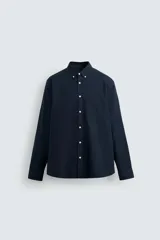 Camisa azul marino de corte regular, confeccionada en tejido de algodón Oxford. Tiene cuello abotonado, manga larga con puños abotonados, bolsillo de parche en el pecho y cierre frontal con botones blancos.