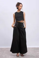 Pantalón negro de tiro alto, corte ancho y largo, con pliegues frontales y pespuntes contrastantes en blanco en la cintura y bolsillos.