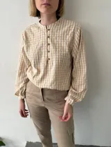 Blusa color beige con estampado a cuadros, cuello mao, mangas largas abullonadas y cierre frontal con botones.