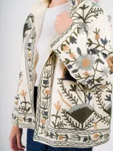 Chaqueta abierta color crema con bordado floral multicolor, corte cuadrado y mangas largas.