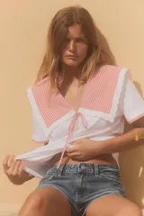 Camiseta blanca de cuello bobo con terminaciones bordadas y detalle de lazo en el delantero. El cuello y las mangas cortas son de tela a cuadros vichy color salmón.