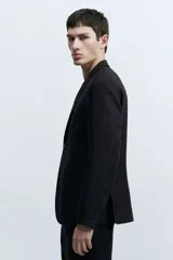 Blazer negro de lino liviano con solapas de muesca finas y ojal decorativo. Modelo de botonadura sencilla con bolsillo superior, bolsillos delanteros con solapa y dos bolsillos en el interior. Cierre de dos botones, botones decorativos en los puños y abertura doble atrás. Corte ajustado que realza el contorno del cuerpo creando una silueta entallada. Forrado.