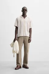 Camisa de manga corta con cuello bowling y corte relaxed fit. Diseño a rayas verticales en tonos beige y blanco. Cierre frontal con botones y bajo con aberturas laterales.