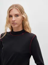 Polera negra de tela rib con cuello alto y mangas largas. Presenta pespuntes rojos en cuello, hombros y puños.