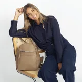 Mochila color beige de símil cuero, con bolsillo frontal de gran capacidad, asa de mano y correas regulables en galón. En su interior tiene dos bolsillos con cierre y uno abierto con división.