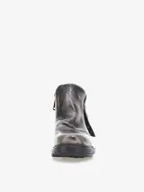 Bota corta de cuero bovino negro con efecto desgastado y envejecido, con detalles en gris claro. Presenta un diseño con solapa frontal que se ajusta con un broche y una cremallera lateral expuesta en el talón. Posee un taco bajo y cuadrado.